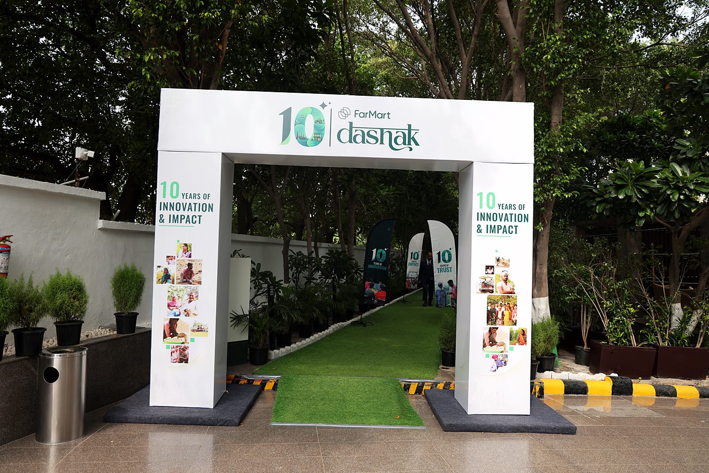 A white entrance arch with the 10 FarMart dashak lockup, leading down a green carpet lined with feather flags.