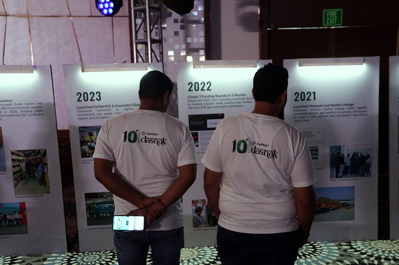 Two people in white Dashak T-shirts, seen from behind, reading timeline boards for 2021, 2022 and 2023.